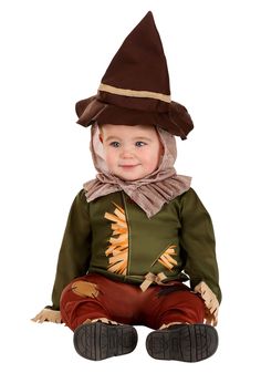 a baby dressed up as a scarecrow sitting on the ground wearing a brown hat and green shirt