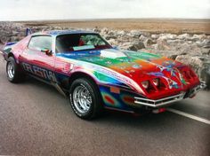 a colorful car is parked on the side of the road in front of some rocks