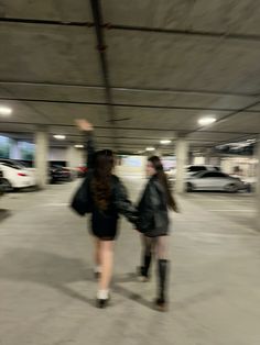 two women walking in an empty parking garage with their backs turned to the camera,