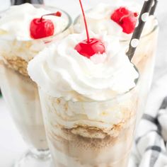 two desserts with whipped cream and cherries on top are sitting in glass cups