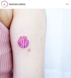 a small tattoo on the arm of a woman with a pink shell and pearl bead