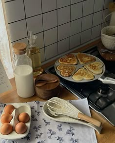 pancakes and eggs on a kitchen counter next to a bottle of milk, whisk sticks, and other cooking utensils