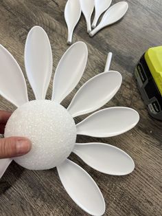 a hand is holding an object made out of spoons and plastic flowers on a wooden table