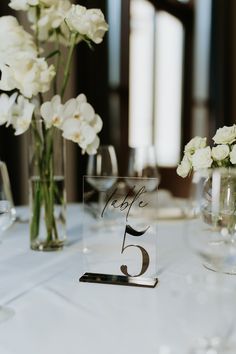 the table numbers are displayed in glass vases with white flowers on top and below them