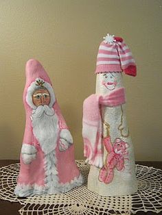 two pink and white dolls on a doily next to each other, one wearing a santa claus hat