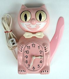 a pink clock with a cat face on it and a cord plugged into the wall