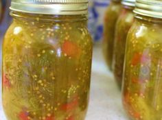 four jars filled with pickles sitting on top of a table