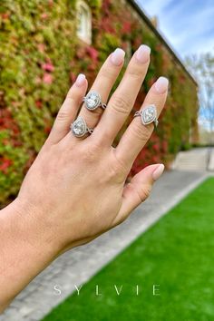 a woman's hand with two rings on her fingers in front of a building