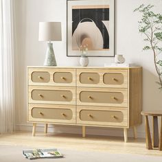 a wooden dresser sitting in front of a window next to a lamp and vase on top of it