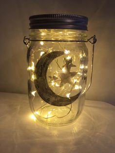 a mason jar filled with fairy lights and a crescent on the inside, sitting on a table