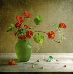 a green vase filled with red flowers sitting on top of a wooden table next to leaves