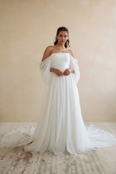 a woman in a white wedding dress standing with her hands on her hips and looking at the camera