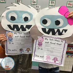 two children holding up paper cutouts with mouths and teeth on them, in front of a classroom wall