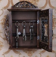 an open wooden box with keys and keychains in it on a floral wallpapered background