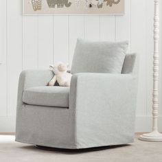 a gray rocking chair with a stuffed animal on it's arm in front of a white wall