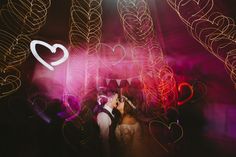 a bride and groom kissing in front of bright lights at their wedding reception with hearts drawn on the wall behind them