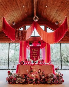 a decorated table with red drapes and flowers on the top is in front of a large window