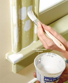 a person holding a paintbrush and painting the side of a window with white paint