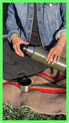 a person sitting on the ground with a water bottle in their hand and a cup next to them