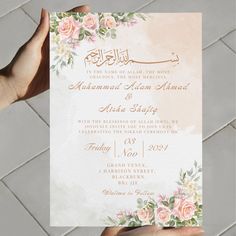 a person holding up a wedding card with flowers on the front and bottom, in arabic