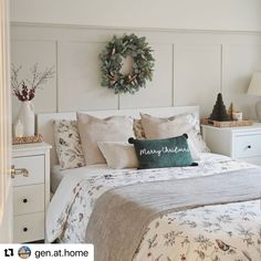 a white bed topped with pillows and blankets next to a christmas wreath on the wall