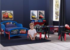 a young boy sitting on the floor in front of his cars bedroom furniture and toys