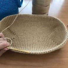 a person is knitting yarn in a basket on a wooden table next to a spool of thread