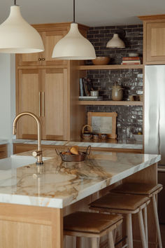 a kitchen with marble counter tops and stools in front of the sink, along with wooden cabinets