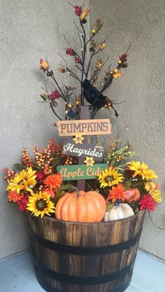 a wooden barrel filled with pumpkins and flowers next to a sign that says pumpkins