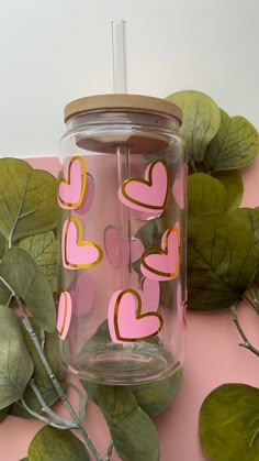 a pink and yellow cup with hearts on it next to some green leafy plants