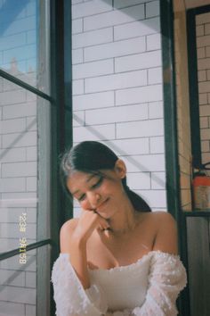 a woman sitting in front of a window with her hand on her face and looking down