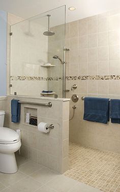 a white toilet sitting next to a walk in shower under a bathroom mirror with blue towels on it