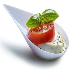 a white plate topped with sliced tomatoes and mozzarella on top of cheese covered in basil