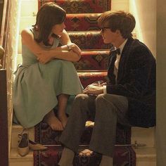 a man and woman sitting on top of a stair case next to each other in front of stairs