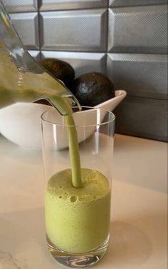 a glass filled with green liquid sitting on top of a counter next to an avocado