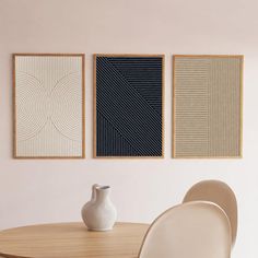 three abstract paintings hang on the wall above a dining room table with chairs and a vase