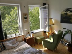 a bed room with a neatly made bed next to two large windows and a painting on the wall