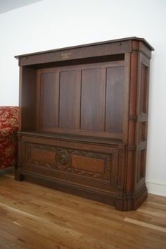 an old wooden cabinet sitting on top of a hard wood floor next to a red couch