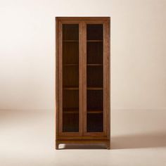 a tall wooden bookcase with glass doors on the front and bottom shelves, against a beige background