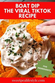 a hand dipping some chips into a white bowl filled with dip and garnished with parsley