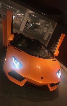 an orange sports car is parked in a garage with its doors open and lights on