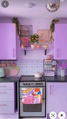 a kitchen with purple cabinets and an oven in the center is filled with pots, pans, and plants