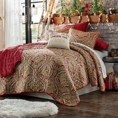 a bed covered in red and gold comforter next to a brick wall with potted plants