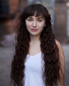 a woman with long brown hair standing in front of a brick building and looking at the camera