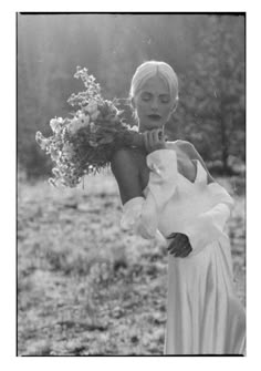 black and white photograph of woman in dress holding flowers with trees in the back ground