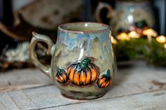 a ceramic mug with pumpkins painted on it sitting on a table next to candles