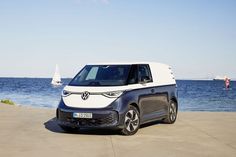 an electric car is parked on the beach near the water and sailboats are in the background