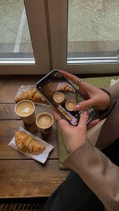 a woman sitting at a table with coffee and pastries in front of her cell phone