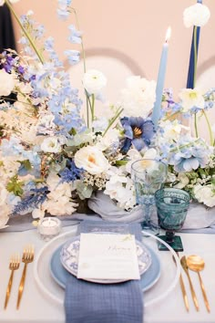 the table is set with blue and white flowers, silverware, and candlesticks