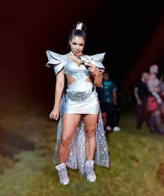 a woman dressed in silver posing for the camera with other people behind her at night